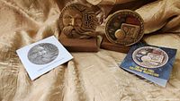 Photo showing both medallions on wooden stands along with their informational cards on a gold fabric background.