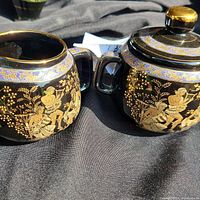 Teapot and creamer showing 24K gold detailed classical artwork on black ceramic