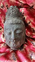 Front view of the Boddhisattva head sculpture showing the facial features and headdress on a red ornamental fabric.