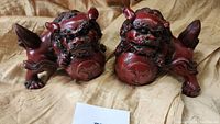 Two Japanese Foo Dog figurines displayed front facing, showing facial and body details including balls under their paws.