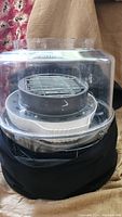 Front view of Nuwave air fryer with clear dome lid and metal rack inside, black cover beneath.