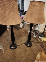 Pair of table lamps with tall dark bases and tan woven shades on carpeted floor.