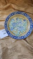 Front view of the porcelain plate showing the blue floral design on a beige background with blue floral border.