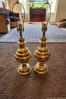 Photo showing two vintage brass table lamps with cord and harp frames, placed on carpeted floor in living room space