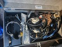 Photo showing an open case containing multiple pairs of over-ear headphones, several coiled cables, connectors, and other audio accessories.