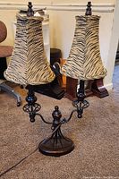 Vintage Hollywood Regency style double lamp with tiger print fabric shades resting on carpeted floor next to office chair and furniture.