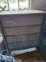 Full front view of a tall wooden console record player with three speaker grills, showing the wood structure and the RCA Victor badge on the front.
