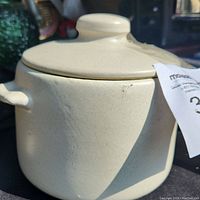 Cream-colored vintage ceramic cooking pot with lid, showing exterior with integrated handles and lid knob.