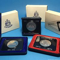 All three Canadian commemorative coins displayed in their original black clamshell holders adorned with blue and red velvet fabric and accompanied by corresponding cream-colored presentation boxes with Canadian insignia.