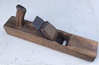 Photo of the antique wooden block plane showing its full length, wooden base, handle and metal blade.