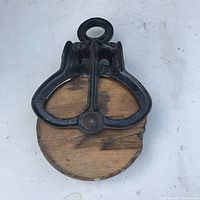 Front view of early wood pulley showing iron frame and wood wheel with missing piece at edge.