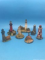 Photo showing seven miniature lighthouse figurines on a blue background, details visible include varied colors and structures.