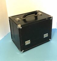 Closed black organizer tote box with silver metal reinforced corners and handle on top.