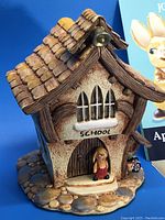 Close-up photo of the ceramic schoolhouse figurine with detailed roof and bunny character in doorway.