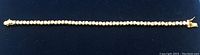 Full-length view of gold-tone tennis bracelet on dark background