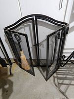 Black cast iron fireplace screen with two mesh doors open and fireplace tools hanging on hooks.