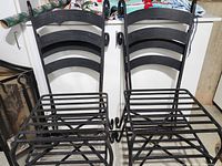 Four black cast iron chairs positioned side by side showing the front and seat design with slatted metal bars and ladder-back frames.