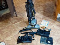 Kirby vacuum cleaner and assorted cleaning attachments including shampooer, brushes, hoses and extension wand laid out on floor.