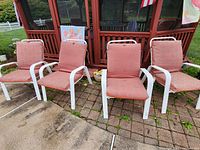 Front view of four white metal outdoor chairs with red cushions arranged in a row on brick and cement patio.