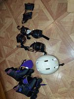 Full set of inline rollerblades, protective gear (wrist, knee, elbow pads) and helmet laid out for viewing
