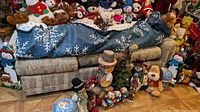 End section of sofa bed covered with blue blanket with snowflake pattern, surrounded by numerous stuffed toys and decorations.