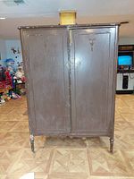 Full front view of the antique wooden cabinet showing the closed double doors with simple carved detail and turned legs