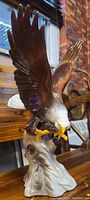Photo showing the falcon with wings extended, perched on a base resembling a tree trunk, with details of the paint and sculpting.