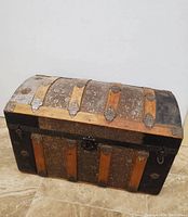 Front view of the vintage wooden dome-top trunk showing wood slats, metal hardware, central lock, and leather side handles.