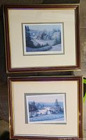 Two framed prints stacked, showing rustic countryside scenes in blue hues with matting and wooden frames.