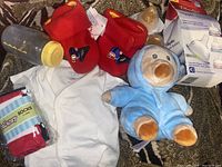 Overview photo of all items in the lot including bottle, booties, socks, T-shirt, plush toy and Playtex nipple box.