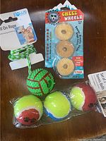 Image showing green and white rope dog toy with ball, Cheez Wheelz pack, spiked green chew toy, and partial tennis balls pack.
