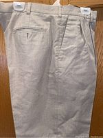 Photo showing men's light beige pants with pleats, side pockets, and a back welt pocket with a button.