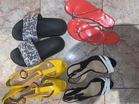 Top-down view of the four pairs of women's shoes showing a mix of styles and colors on a stone floor.
