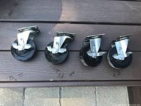 Several 4-inch rubber wheel castors with metal swivel brackets and locking mechanisms shown from side angle on wooden background.