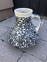Side view of ceramic vase showing black and white floral pattern and handle with repair.