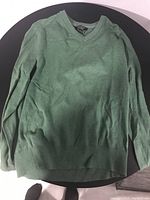Image of a green long sleeve V-neck men's sweater made from cashmere, laid flat on a round dark surface.
