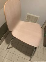 Side angle view of birch colored Ikea chair showing curved plywood seat and backrest with shiny chrome legs on tiled floor.