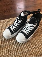 Black and white women's high top running shoes on a rug, side-by-side with white laces and rubber soles visible.