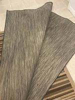 Photo of IKEA indoor outdoor carpet showing grey striped pattern and curled edge.