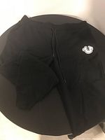 Full view of mens black jogging pants with drawstring and logo on left thigh.