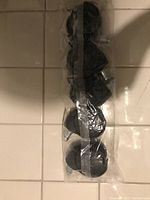 Front view of 5 black office chair wheels in sealed transparent plastic bag taped shut, laid on tiled floor.