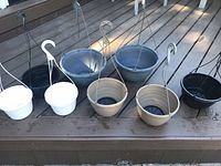 Photo showing 8 plastic hanging baskets in different colors and sizes on a wooden deck.
