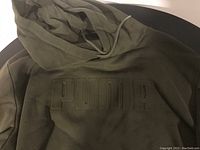 Close-up of the PUMA logo embossed on the front chest area of the army green hoodie.