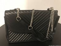 Front view of black pleather purse showing diagonal ribbed pattern and silver chain handle.