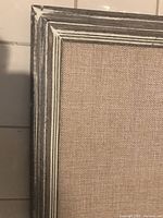 Close-up of corner showing distressed wood frame and burlap fabric surface.