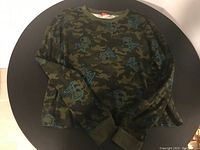 Front laid flat view of green camo long sleeve shirt with blue Snoopy allover print