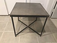 Front view of one square side table showing brown tile top and black steel frame.
