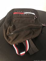 Front and side view of the Tommy Hilfiger backpack showing front zippered pocket and logo