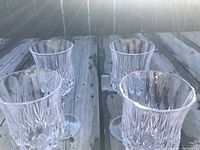 Four clear wine glasses with crystal-cut pattern shown in a group on a wooden surface.