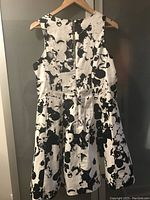 Back view of black and white floral sleeveless dress on hanger showing zipper and flared skirt